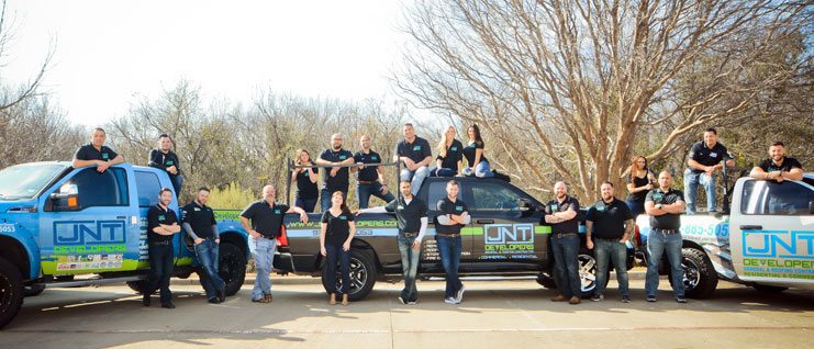 The JNT team all standing around 3 trucks with the the JNT logo on them